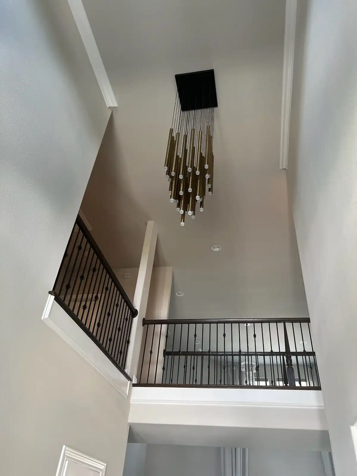 Brass tube pendant chandelier installed in a two storey stairwell