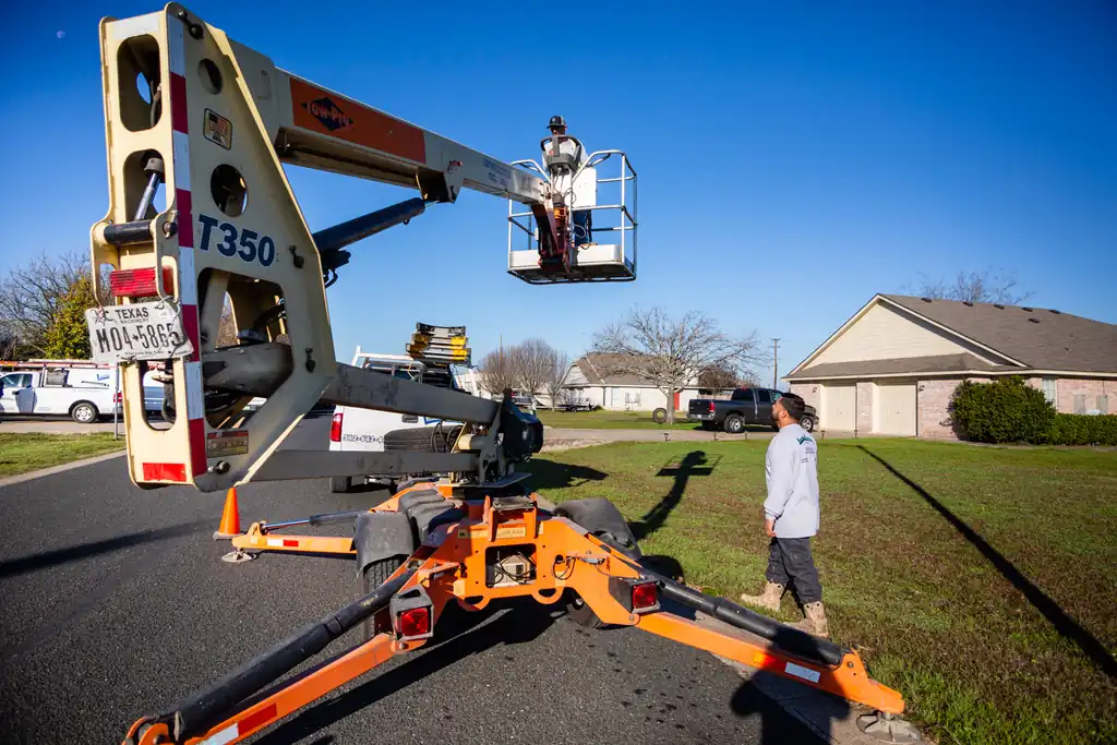 Lightning Electrical bucket lift truck raised to a pole-mounted light while a second technician works from the ground